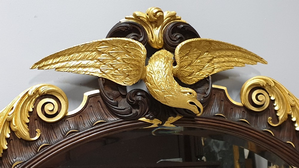 An ornate oval mahogany wall mirror featuring a carved eagle crest, parcel gilt acanthus leaf borders, side lattice panels, and a central classical mask motif at the base. View V