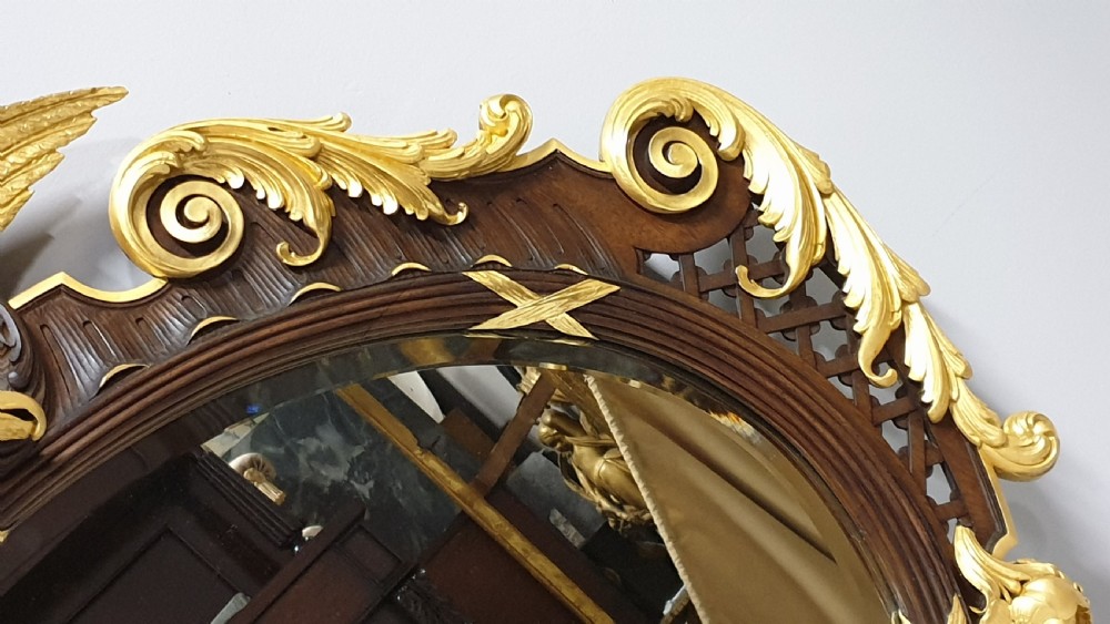 An ornate oval mahogany wall mirror featuring a carved eagle crest, parcel gilt acanthus leaf borders, side lattice panels, and a central classical mask motif at the base. View VI