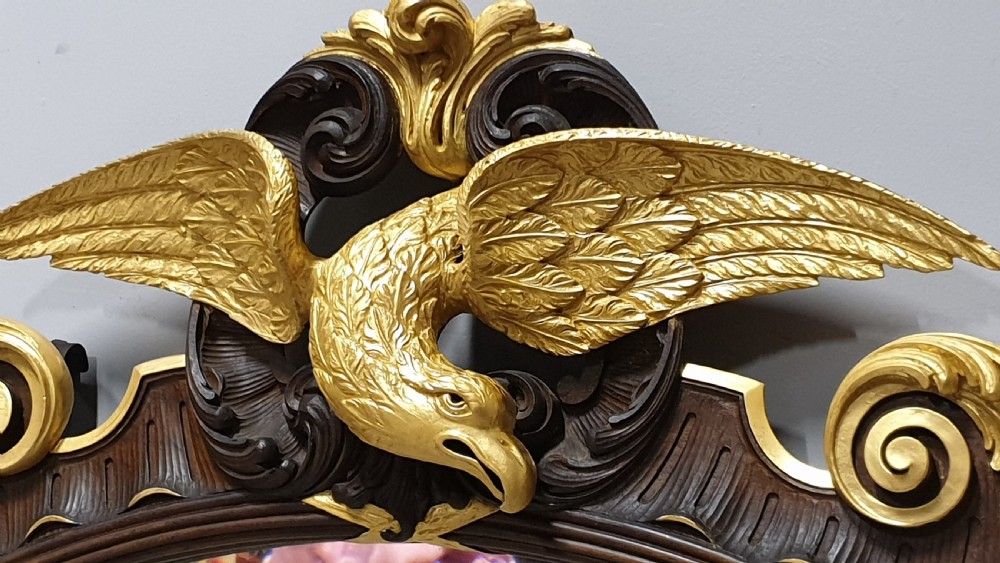 An ornate oval mahogany wall mirror featuring a carved eagle crest, parcel gilt acanthus leaf borders, side lattice panels, and a central classical mask motif at the base. View IX