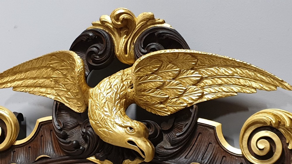An ornate oval mahogany wall mirror featuring a carved eagle crest, parcel gilt acanthus leaf borders, side lattice panels, and a central classical mask motif at the base. View X