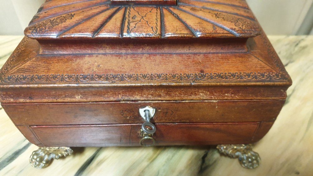 A Regency period tooled brown leather sewing box featuring a sarcophagus-shaped lid, cast brass claw feet, side ring handles, and a lower drawer. View V