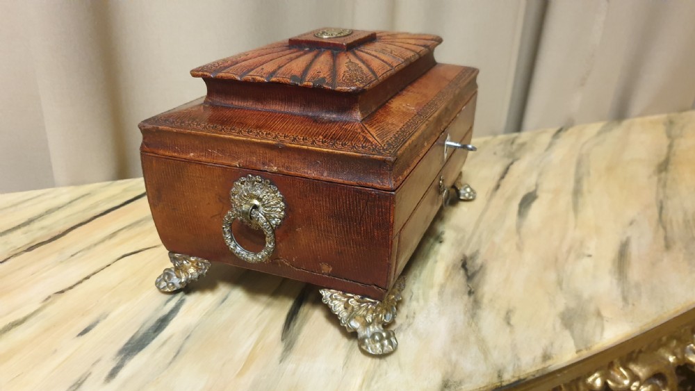 A Regency period tooled brown leather sewing box featuring a sarcophagus-shaped lid, cast brass claw feet, side ring handles, and a lower drawer. View X
