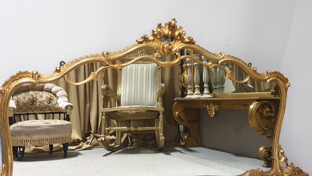 A wide French Rococo style gilt overmantel mirror with an ornate carved central crest and sweeping serpentine gold frame. View II