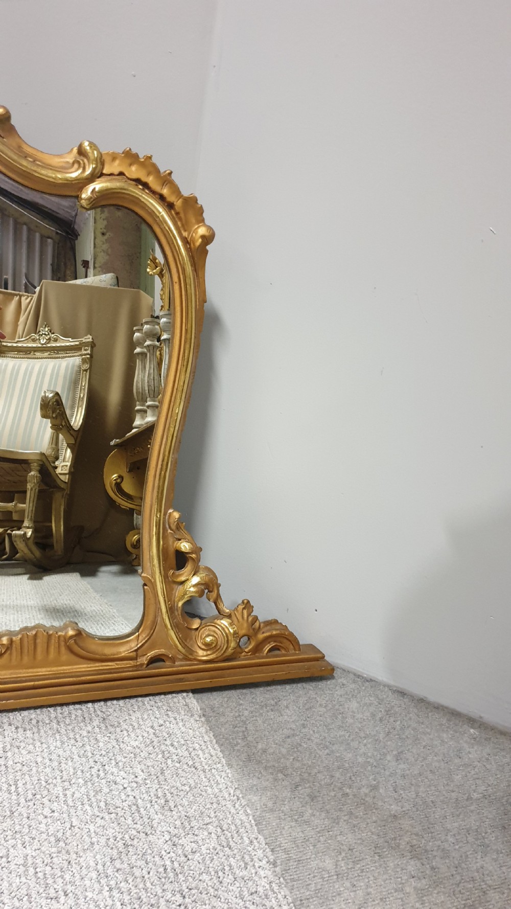 A wide French Rococo style gilt overmantel mirror with an ornate carved central crest and sweeping serpentine gold frame. View IV