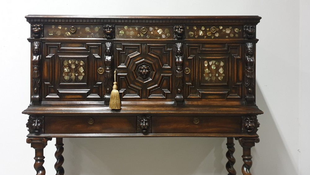 A dark carved walnut cabinet on a stand featuring mother of pearl inlay, carved lion mask details, geometric door panels, and barley twist legs with a stretcher. View III