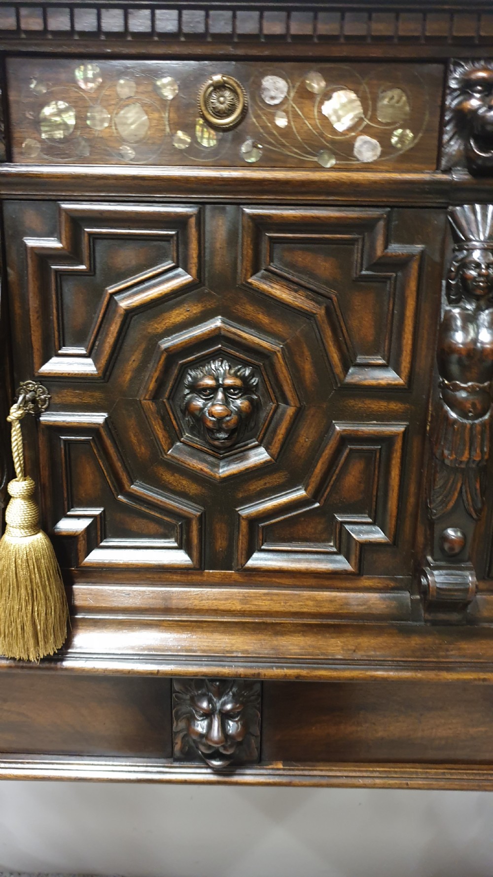 A dark carved walnut cabinet on a stand featuring mother of pearl inlay, carved lion mask details, geometric door panels, and barley twist legs with a stretcher. View V