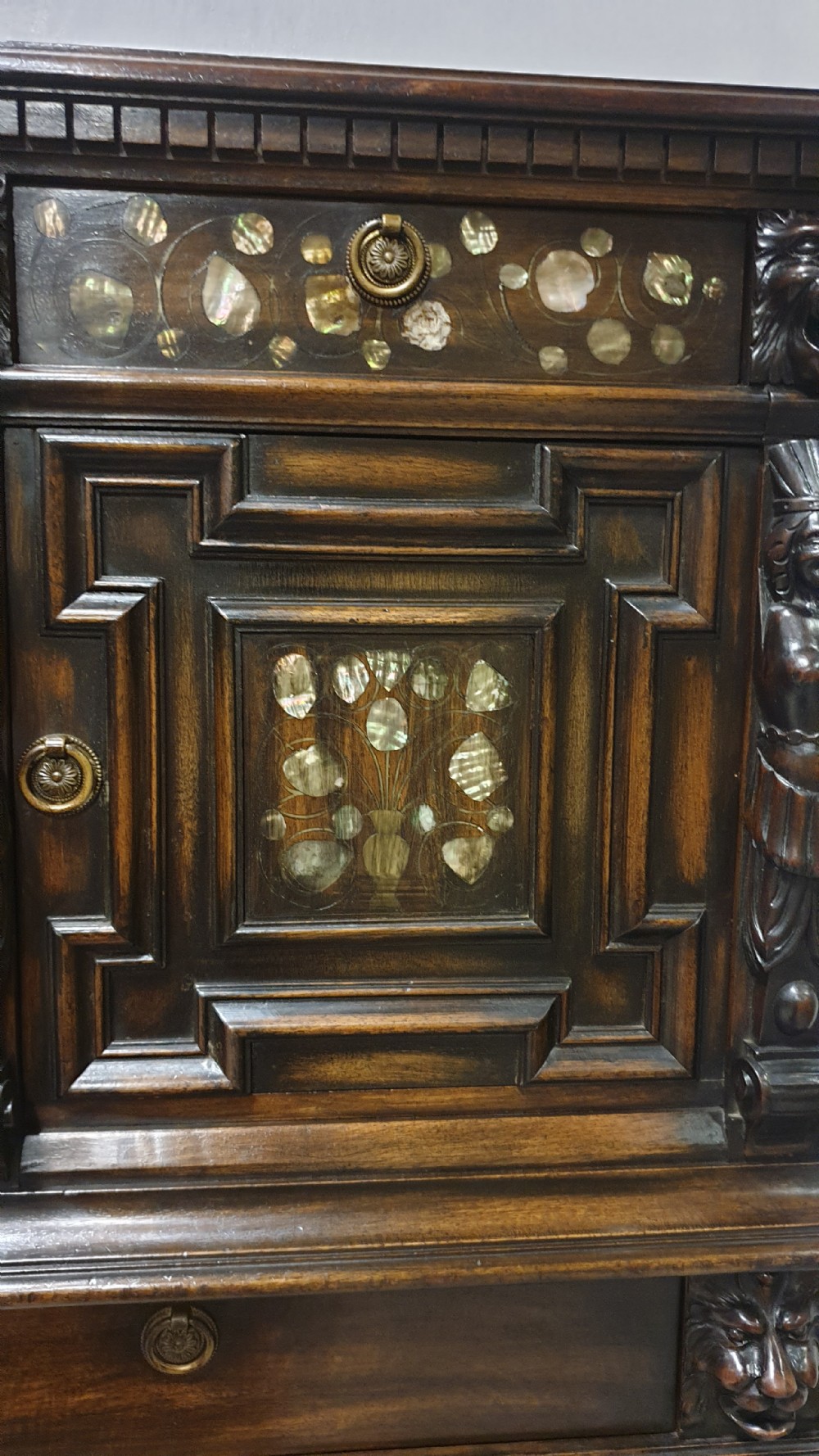 A dark carved walnut cabinet on a stand featuring mother of pearl inlay, carved lion mask details, geometric door panels, and barley twist legs with a stretcher. View VI