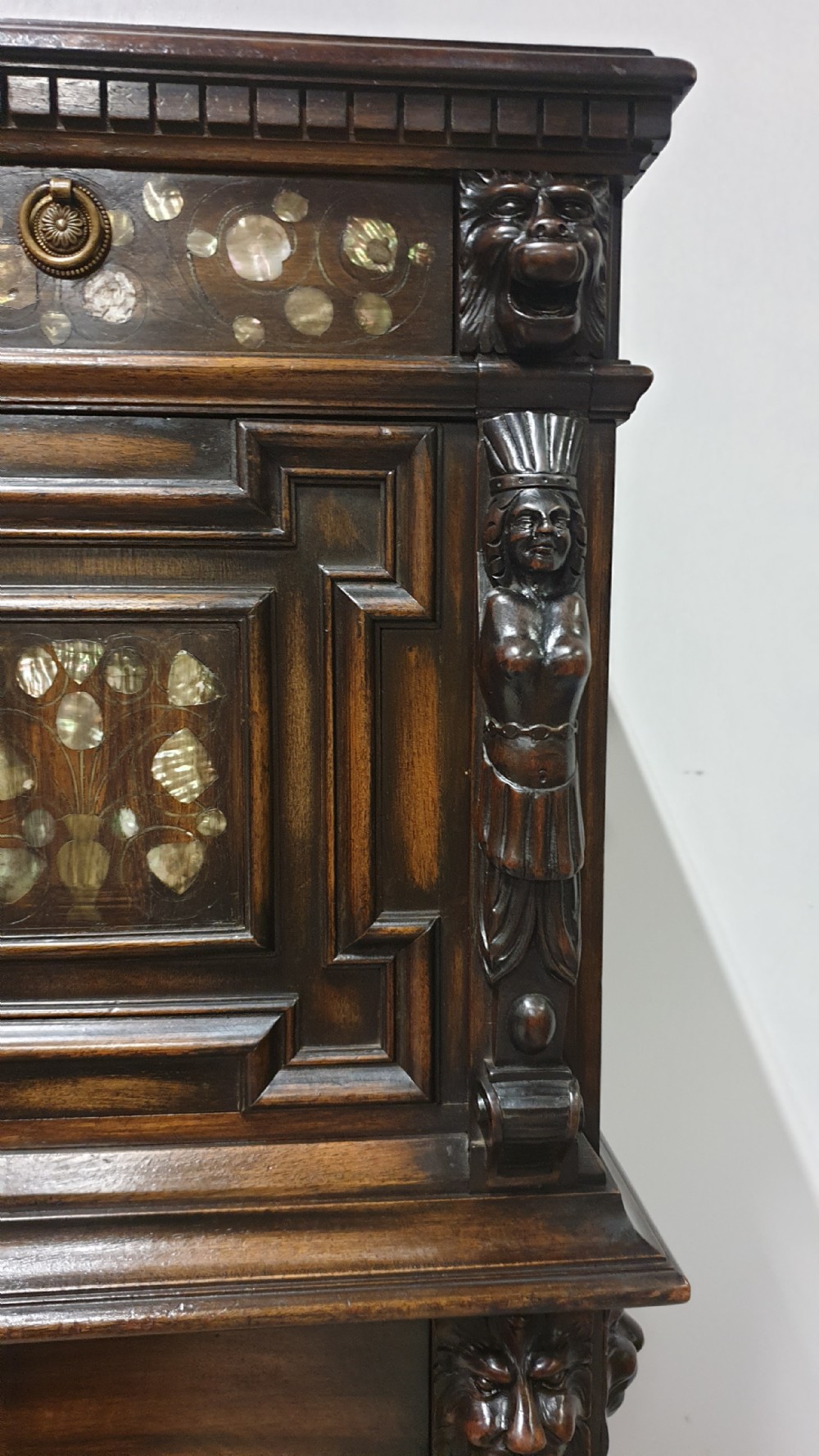 A dark carved walnut cabinet on a stand featuring mother of pearl inlay, carved lion mask details, geometric door panels, and barley twist legs with a stretcher. View VII