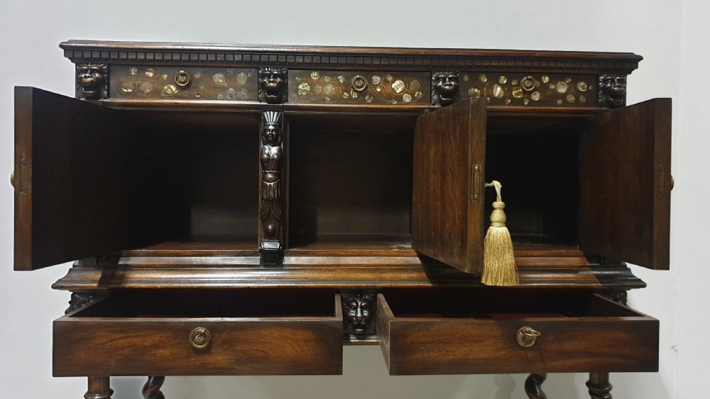 A dark carved walnut cabinet on a stand featuring mother of pearl inlay, carved lion mask details, geometric door panels, and barley twist legs with a stretcher. View XI
