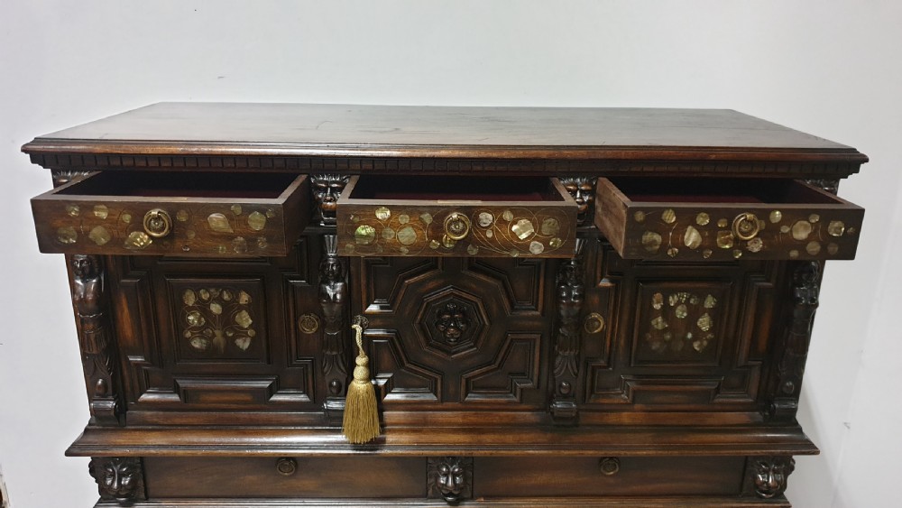 A dark carved walnut cabinet on a stand featuring mother of pearl inlay, carved lion mask details, geometric door panels, and barley twist legs with a stretcher. View XII
