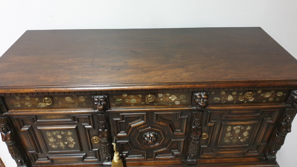 A dark carved walnut cabinet on a stand featuring mother of pearl inlay, carved lion mask details, geometric door panels, and barley twist legs with a stretcher. View XIV