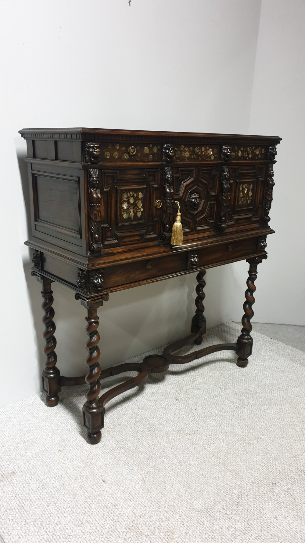 A dark carved walnut cabinet on a stand featuring mother of pearl inlay, carved lion mask details, geometric door panels, and barley twist legs with a stretcher. View XVI