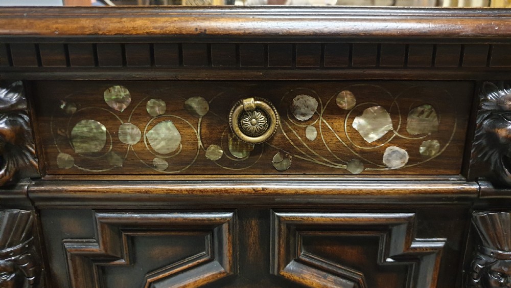 A dark carved walnut cabinet on a stand featuring mother of pearl inlay, carved lion mask details, geometric door panels, and barley twist legs with a stretcher. View XIX