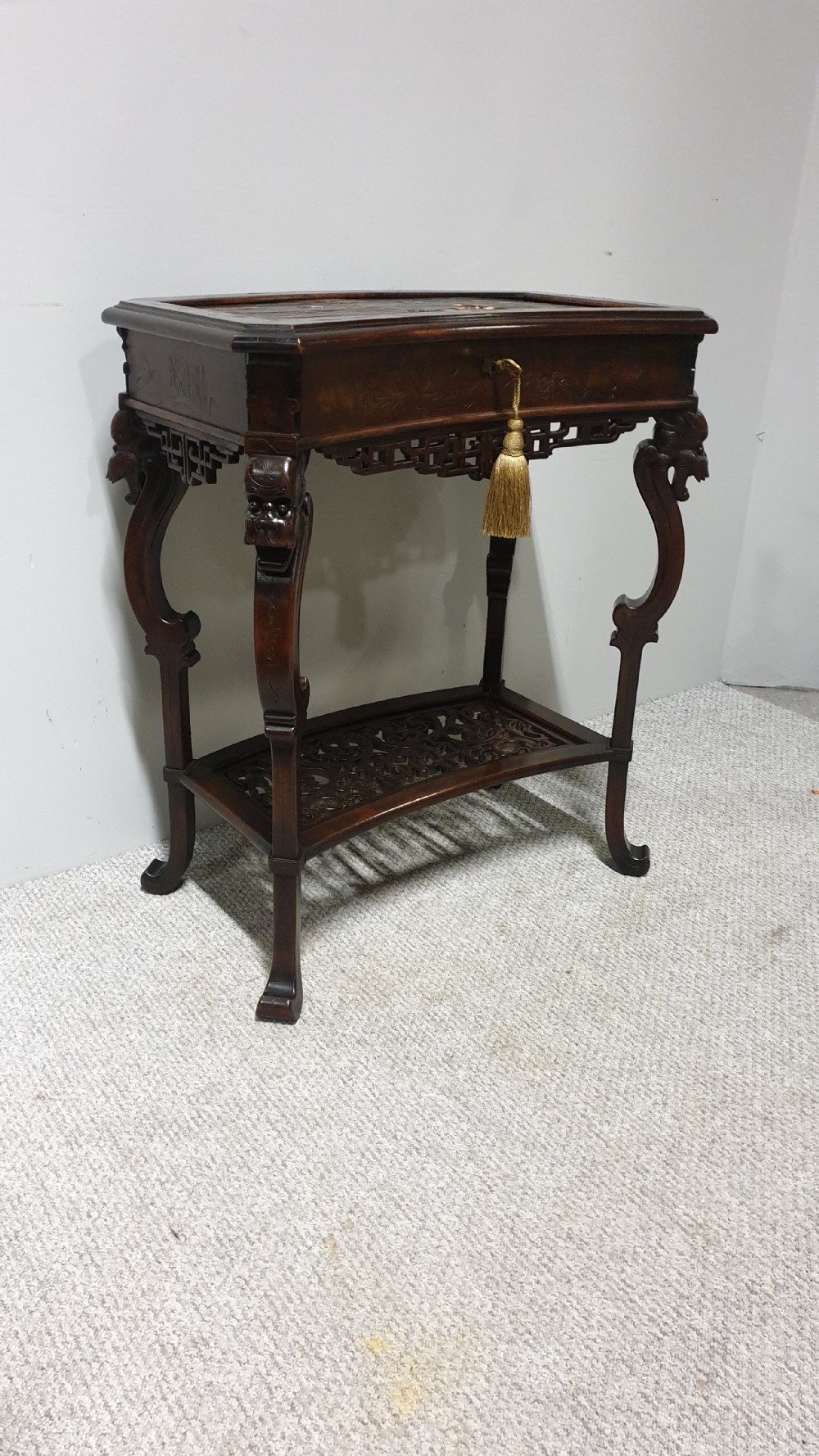 A dark brown Japanese lacquered work table featuring carved dragon head knees, a pierced apron, and a lower openwork shelf.