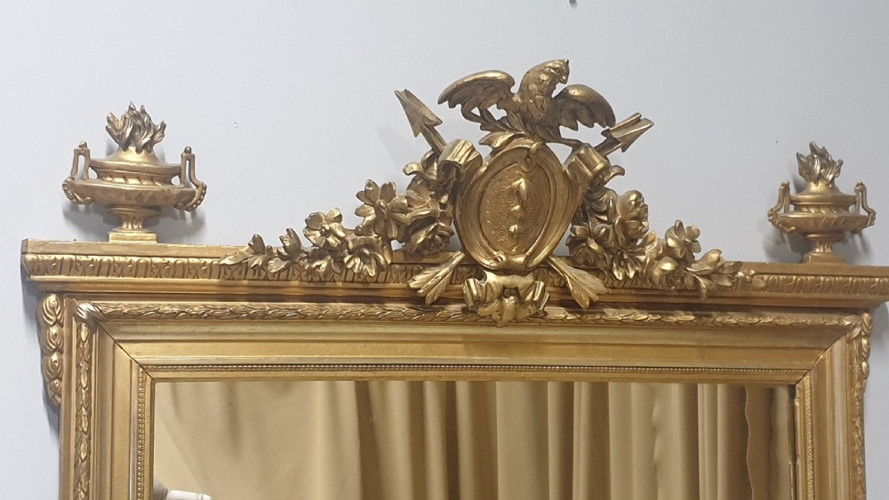 A tall rectangular French giltwood mirror featuring an ornate eagle crest flanked by urn finials and moulded frame detailing. View III
