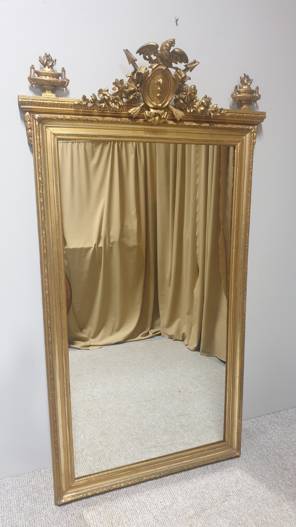 A tall rectangular French giltwood mirror featuring an ornate eagle crest flanked by urn finials and moulded frame detailing. View VI