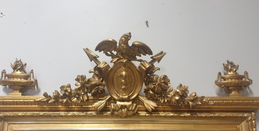 A tall rectangular French giltwood mirror featuring an ornate eagle crest flanked by urn finials and moulded frame detailing. View VII