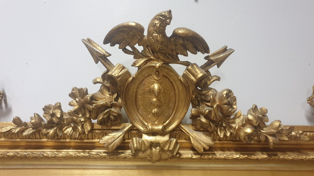 A tall rectangular French giltwood mirror featuring an ornate eagle crest flanked by urn finials and moulded frame detailing. View VIII