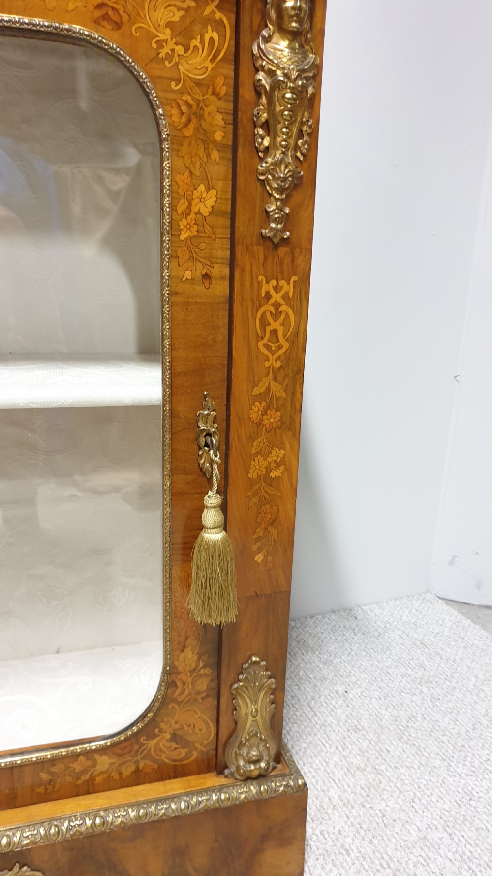 A Victorian walnut pier cabinet featuring floral marquetry inlays, gilt metal ormolu mounts, and a single glazed door opening to light-coloured shelves. View VIII
