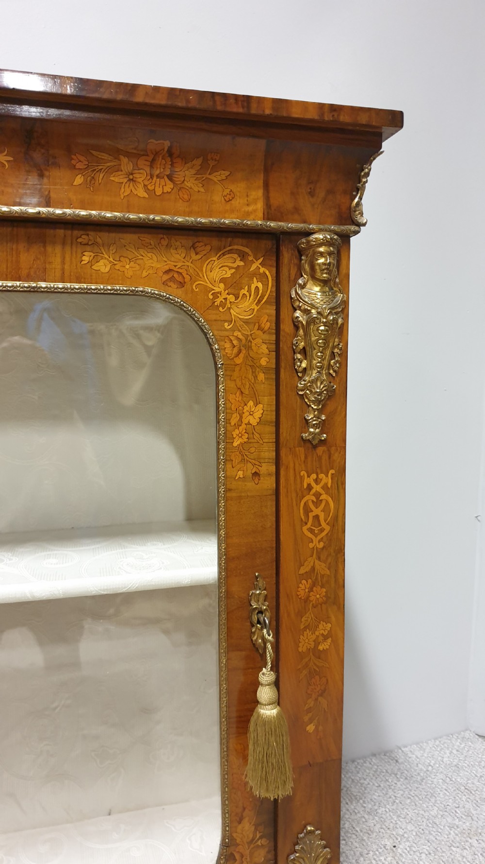 A Victorian walnut pier cabinet featuring floral marquetry inlays, gilt metal ormolu mounts, and a single glazed door opening to light-coloured shelves. View IX