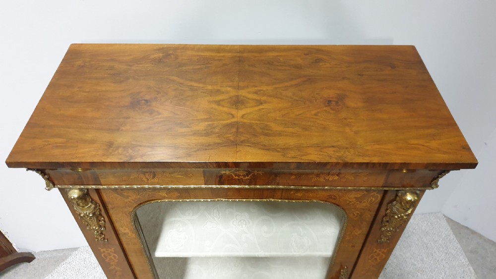 A Victorian walnut pier cabinet featuring floral marquetry inlays, gilt metal ormolu mounts, and a single glazed door opening to light-coloured shelves. View X