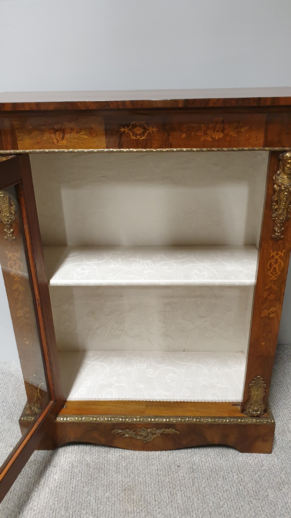 A Victorian walnut pier cabinet featuring floral marquetry inlays, gilt metal ormolu mounts, and a single glazed door opening to light-coloured shelves. View XII