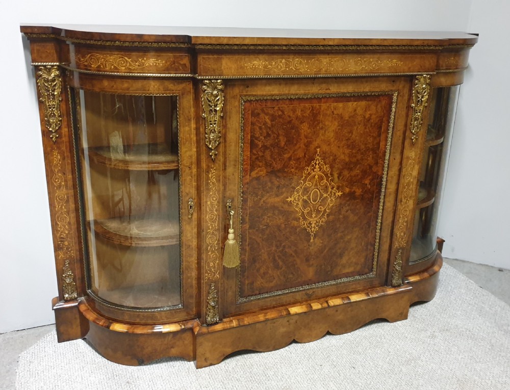A Victorian burr walnut credenza featuring a central inlaid cupboard door flanked by two curved glazed display side cabinets and decorative gilt ormolu mounts. View XV