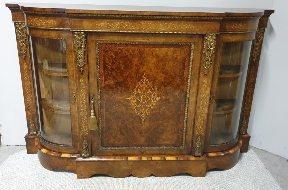 A Victorian burr walnut credenza featuring a central inlaid cupboard door flanked by two curved glazed display side cabinets and decorative gilt ormolu mounts. View XVI