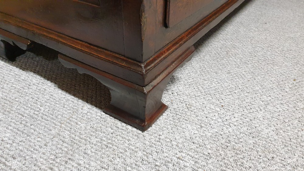 A dark oak Georgian Lancashire coffer featuring nine fielded panel drawer fronts with brass swan-neck handles and a hinged top lid resting on ogee bracket feet. View IX