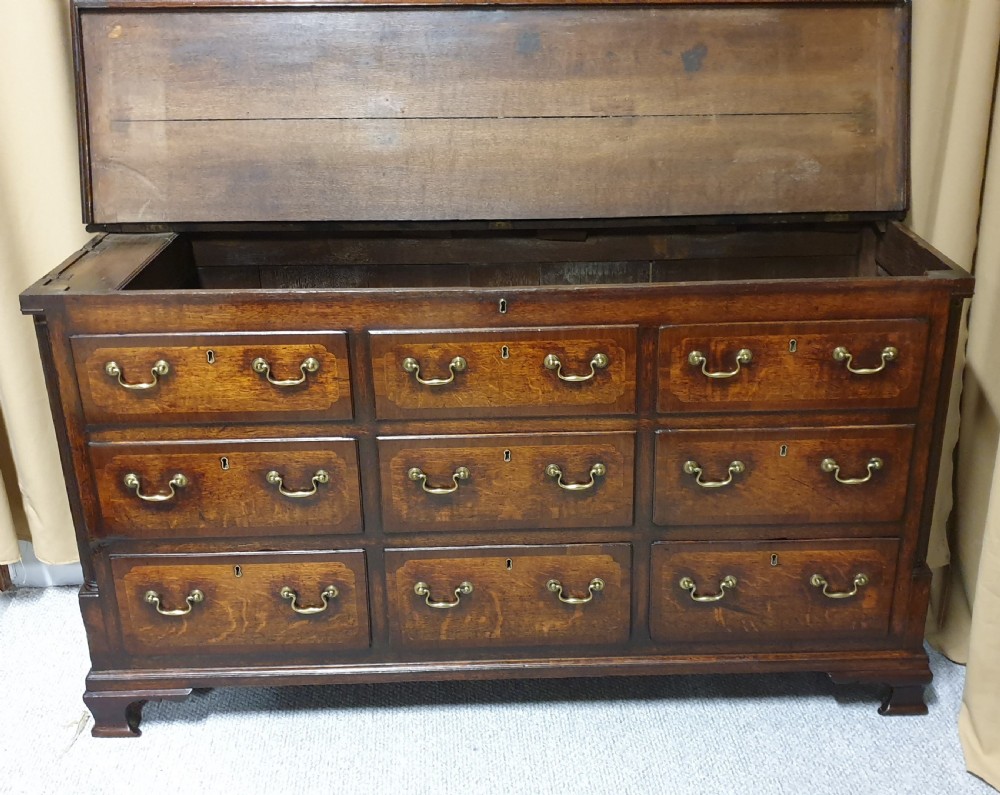 A dark oak Georgian Lancashire coffer featuring nine fielded panel drawer fronts with brass swan-neck handles and a hinged top lid resting on ogee bracket feet. View XII