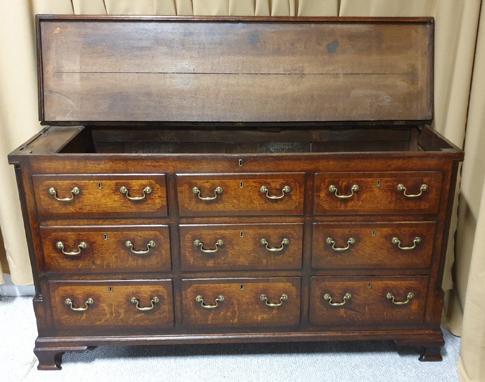 A dark oak Georgian Lancashire coffer featuring nine fielded panel drawer fronts with brass swan-neck handles and a hinged top lid resting on ogee bracket feet. View XIII