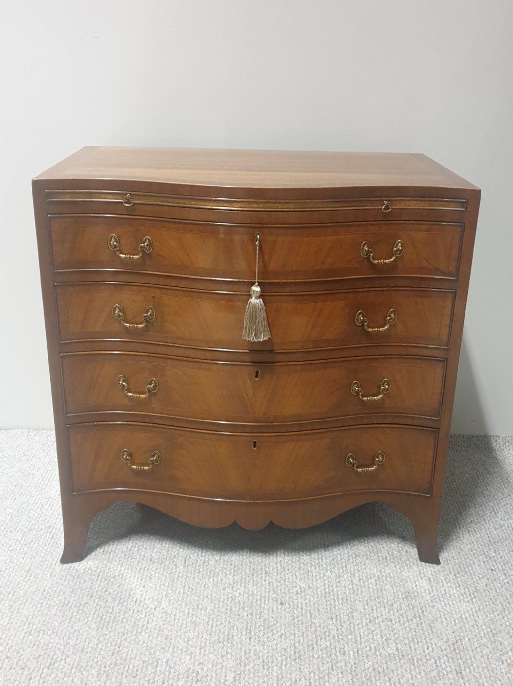 A small mahogany chest of drawers featuring a curved serpentine front, four graduated drawers with brass handles, and bracket feet.
