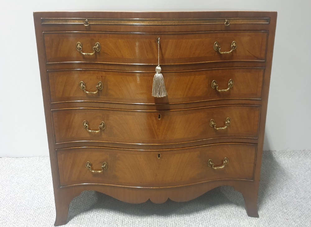 A small mahogany chest of drawers featuring a curved serpentine front, four graduated drawers with brass handles, and bracket feet. View II