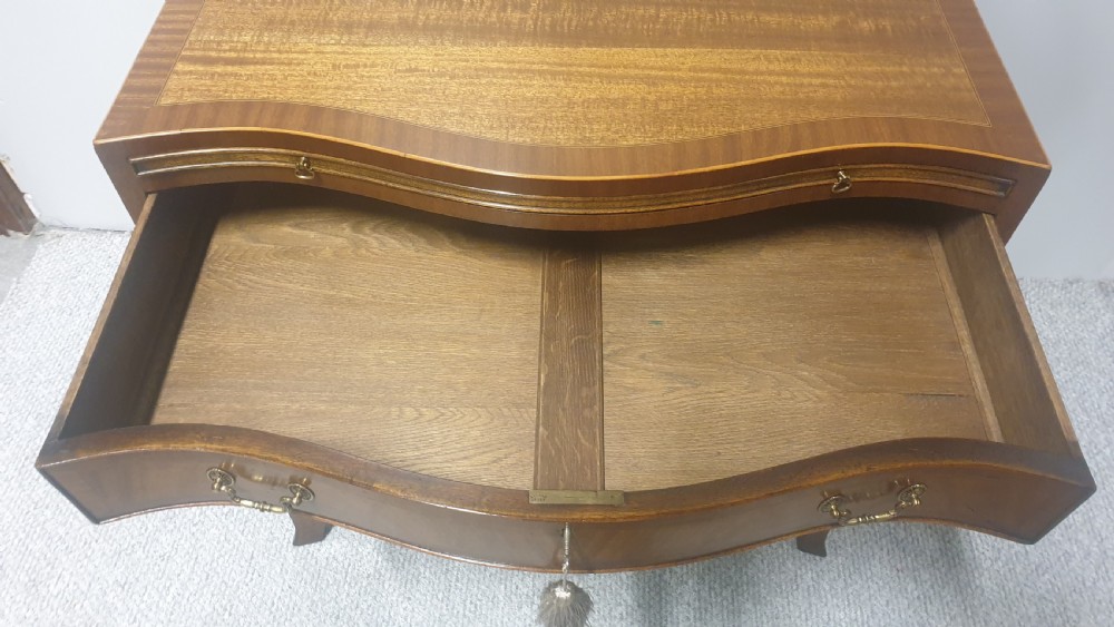 A small mahogany chest of drawers featuring a curved serpentine front, four graduated drawers with brass handles, and bracket feet. View VIII