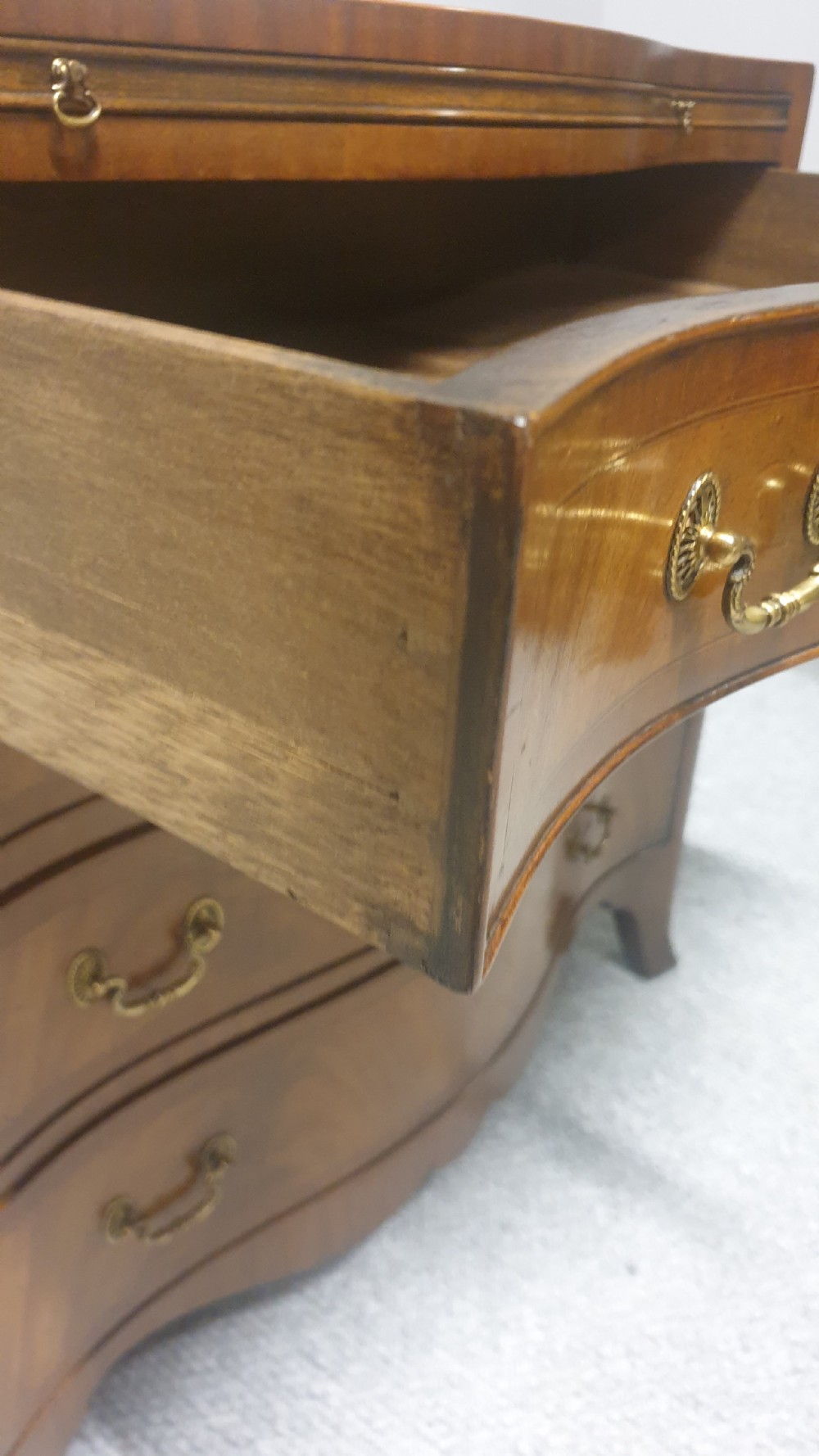 A small mahogany chest of drawers featuring a curved serpentine front, four graduated drawers with brass handles, and bracket feet. View IX