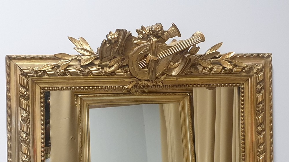 A tall rectangular French giltwood pier mirror topped with an ornate carved crest featuring a musical lyre and foliage. View II