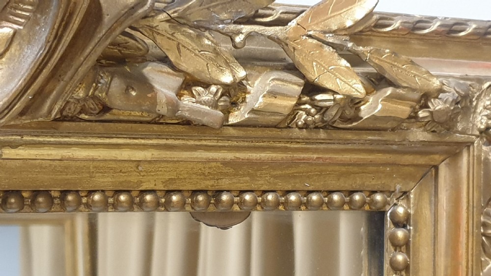 A tall rectangular French giltwood pier mirror topped with an ornate carved crest featuring a musical lyre and foliage. View VI