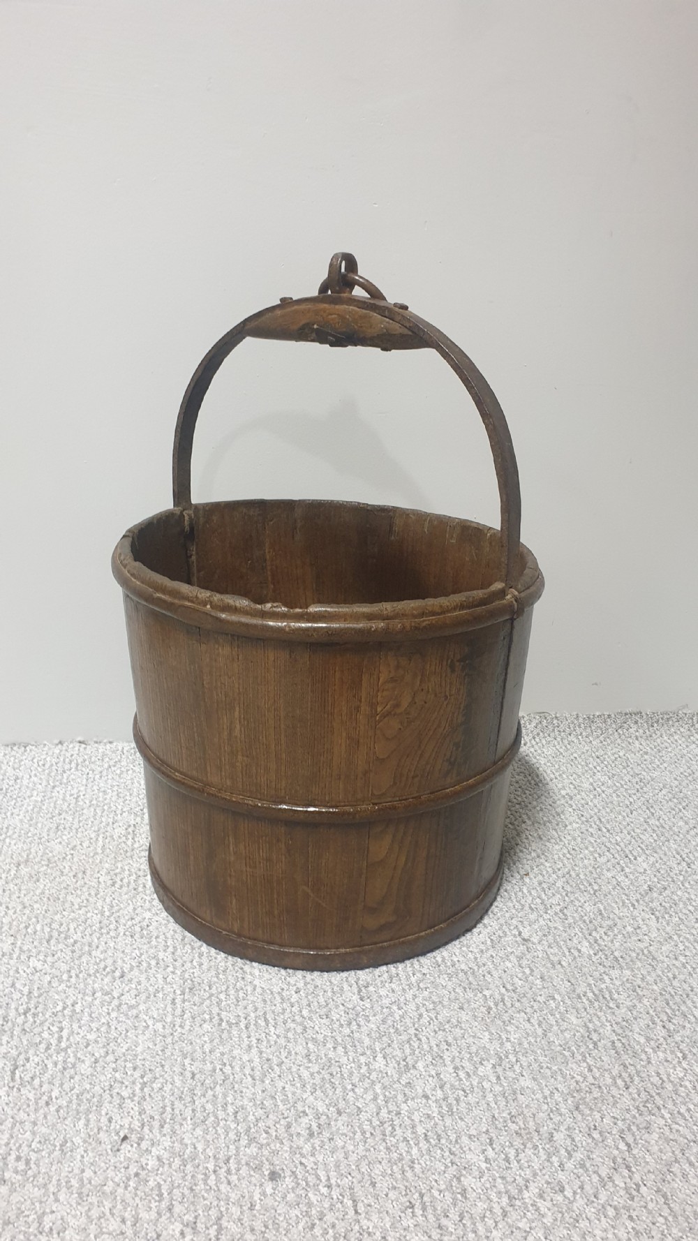 A staved dark oak cylindrical bucket bound with iron hoops and featuring a central overhead iron handle.