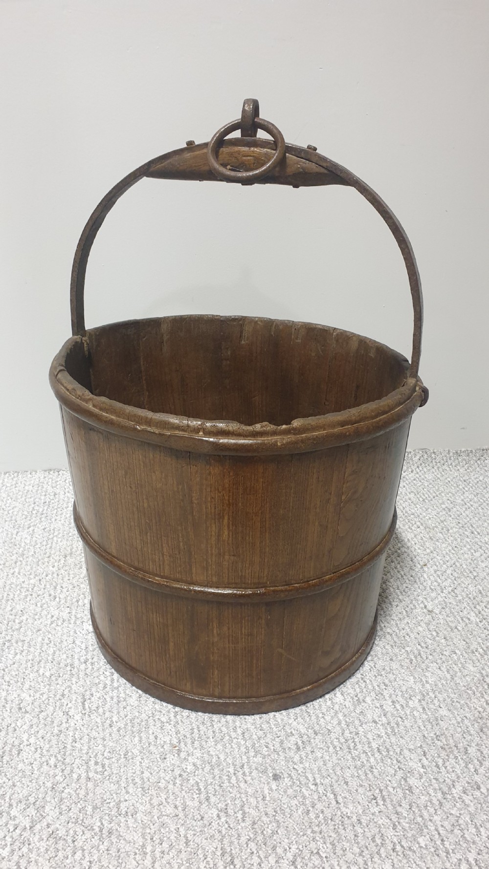 A staved dark oak cylindrical bucket bound with iron hoops and featuring a central overhead iron handle. View V