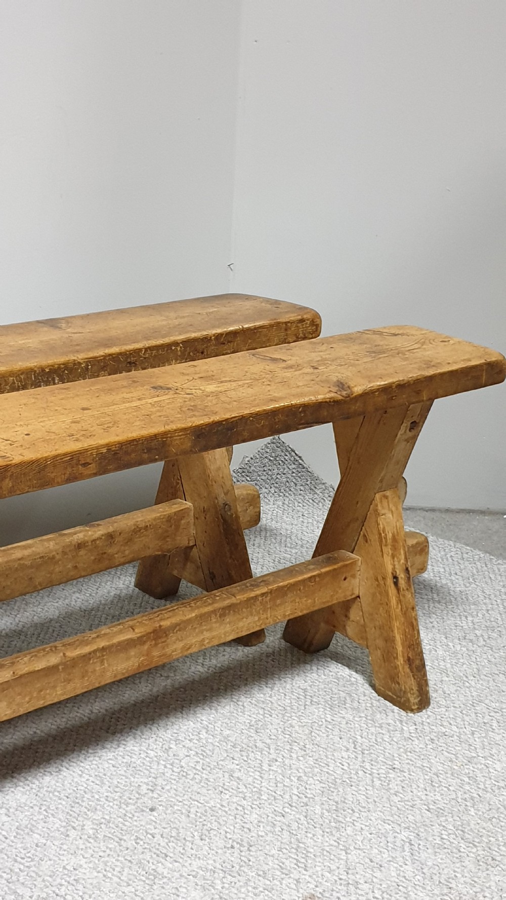 A pair of long rustic pine trestle benches featuring A-frame legs and exposed wooden stretchers. View II