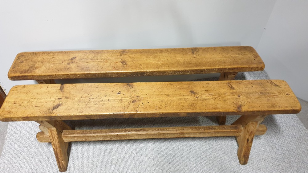 A pair of long rustic pine trestle benches featuring A-frame legs and exposed wooden stretchers. View III