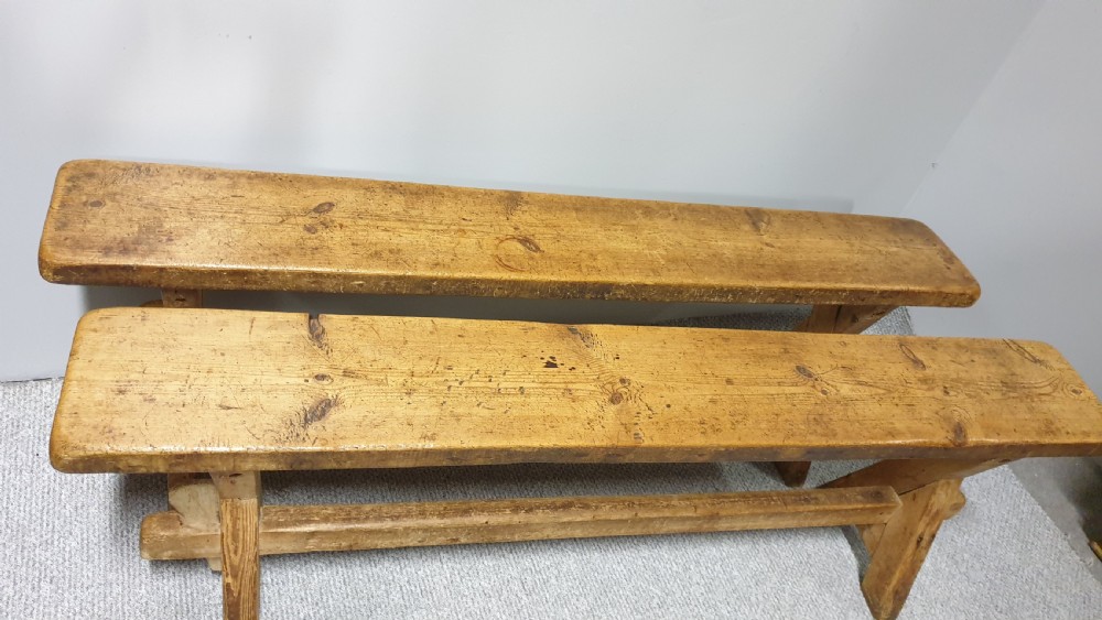 A pair of long rustic pine trestle benches featuring A-frame legs and exposed wooden stretchers. View IV