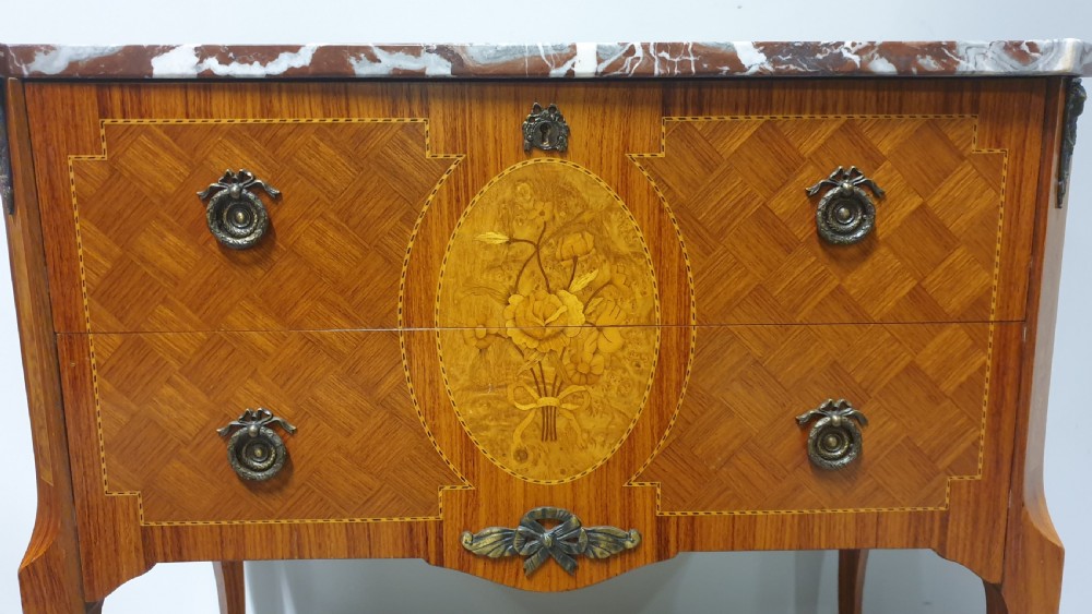 A French-style wooden commode with two drawers, featuring a white and red veined marble top, central floral marquetry medallion, bronze handles, and cabriole legs. View III