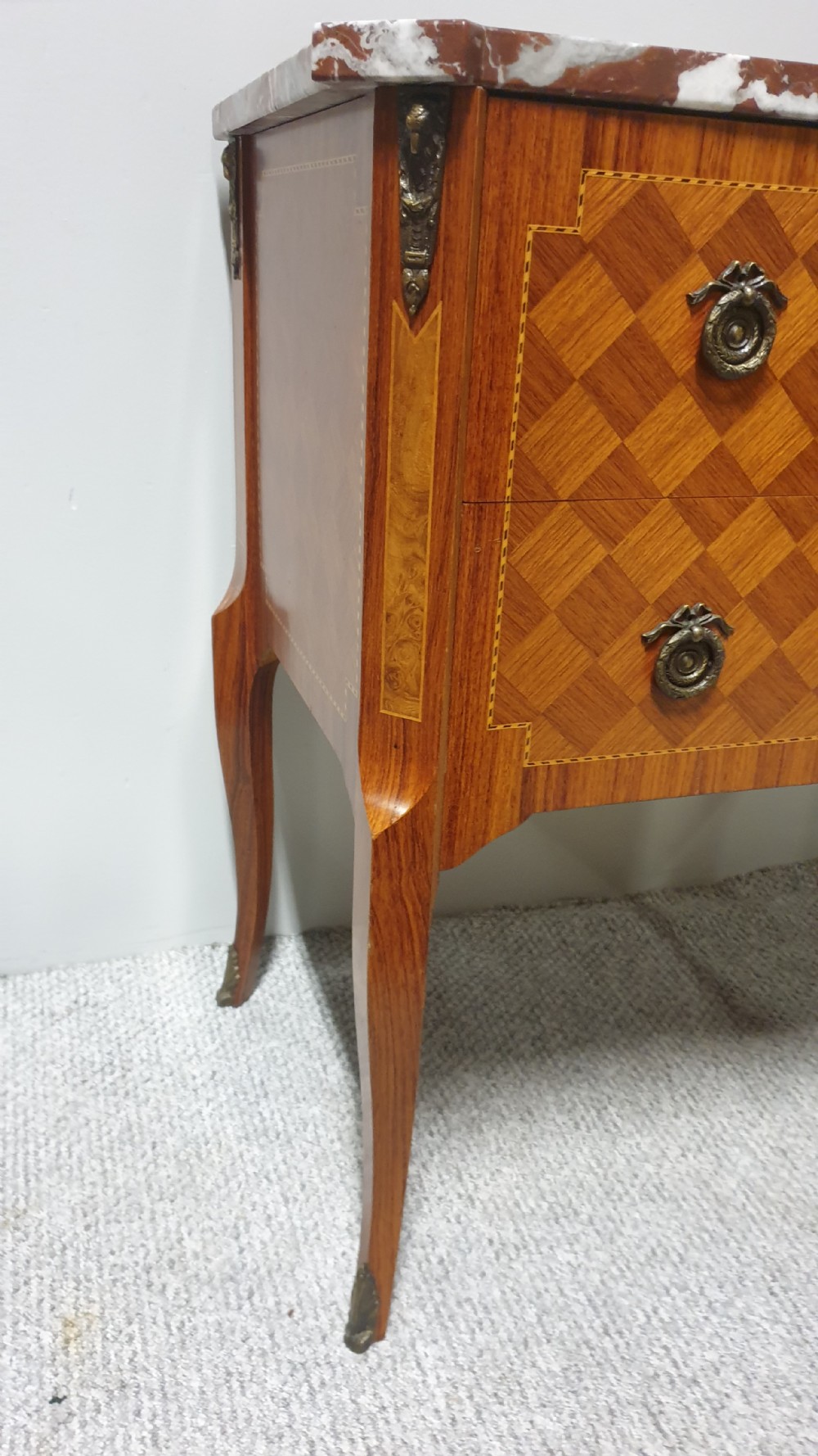 A French-style wooden commode with two drawers, featuring a white and red veined marble top, central floral marquetry medallion, bronze handles, and cabriole legs. View V