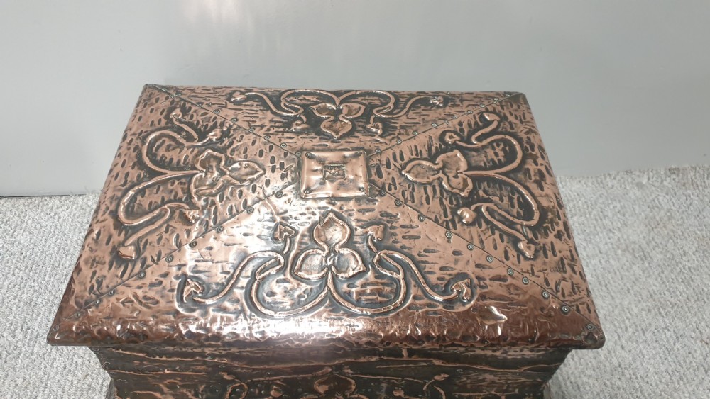 An antique rectangular copper fireside box featuring a hinged lid, hammered repousse foliate motifs, flared sides, and small bun feet. View IV