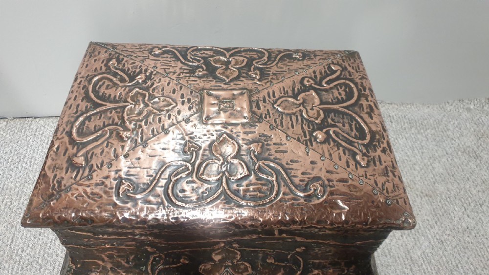 An antique rectangular copper fireside box featuring a hinged lid, hammered repousse foliate motifs, flared sides, and small bun feet. View VII