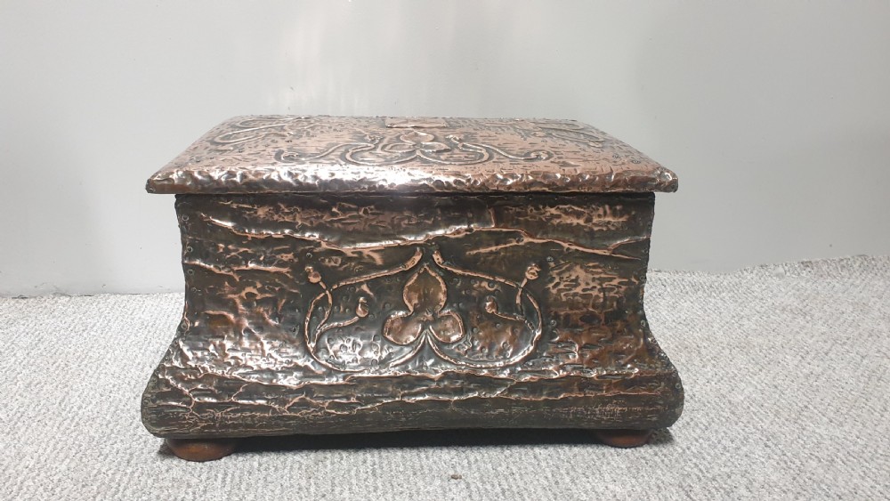 An antique rectangular copper fireside box featuring a hinged lid, hammered repousse foliate motifs, flared sides, and small bun feet. View VIII