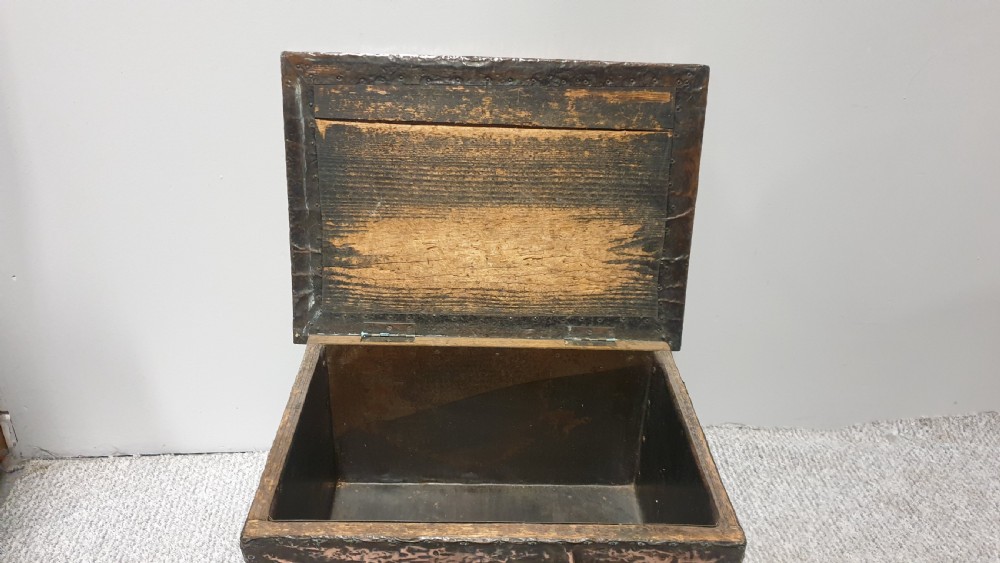 An antique rectangular copper fireside box featuring a hinged lid, hammered repousse foliate motifs, flared sides, and small bun feet. View IX