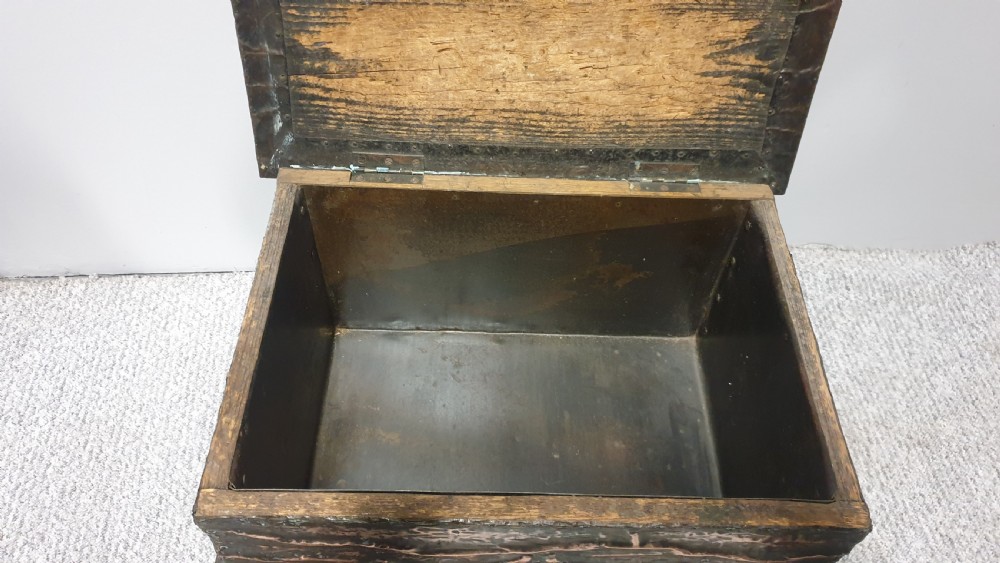 An antique rectangular copper fireside box featuring a hinged lid, hammered repousse foliate motifs, flared sides, and small bun feet. View X