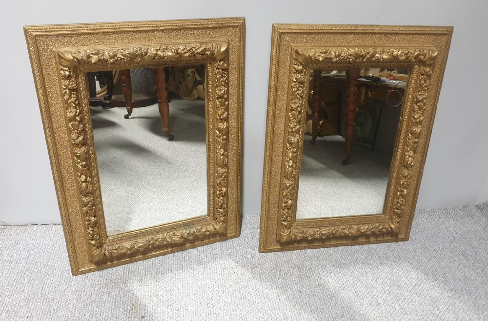 A matching pair of rectangular Victorian wall mirrors featuring ornate floral gesso moulding and a burnished gold finish.